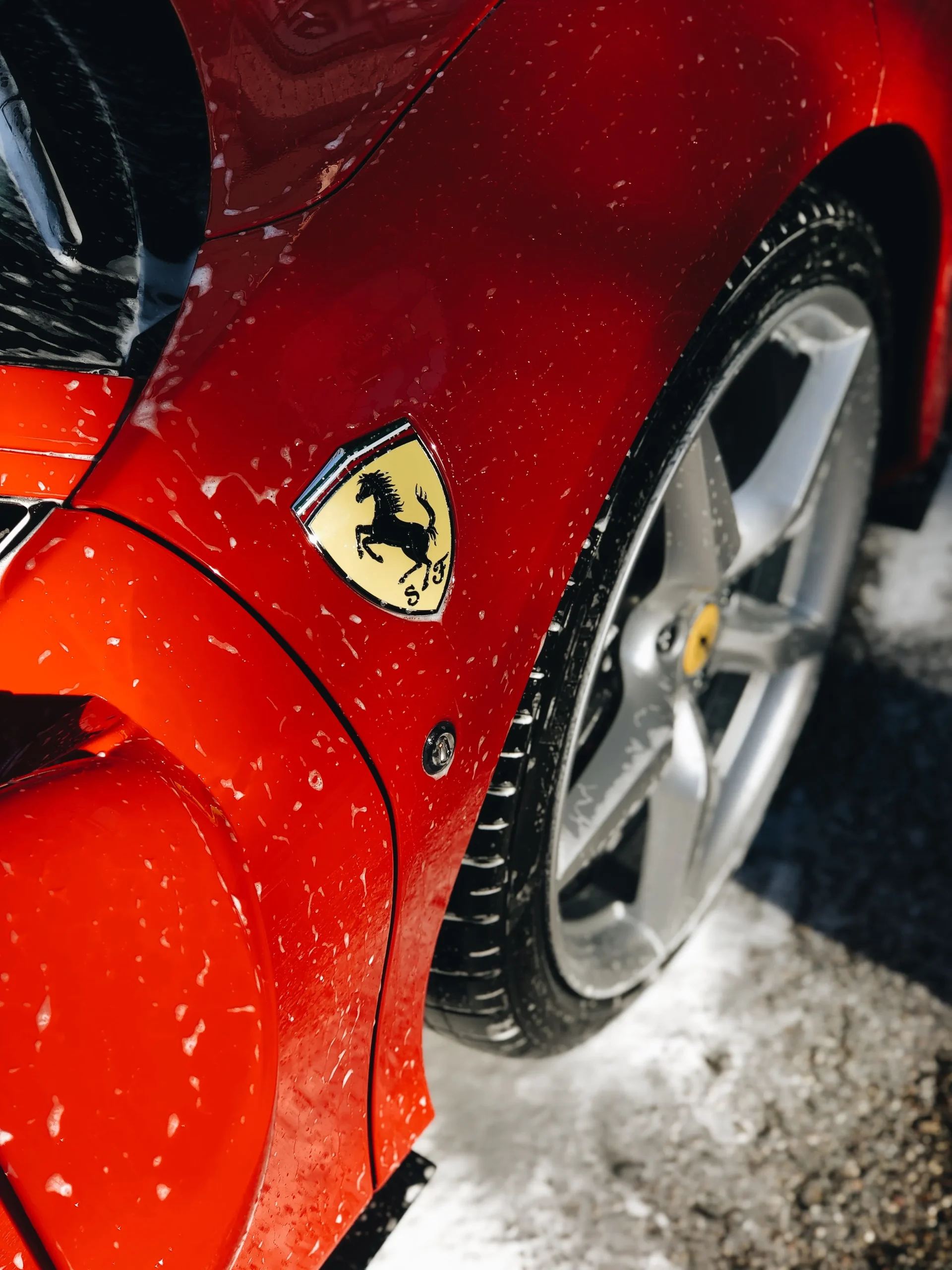 Roter Ferrari mit Wassertropfen auf Kotflügel und Felge bei der Handwäsche